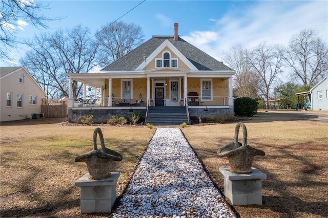 view of front facade featuring covered porch, roof with shingles, and a front yard