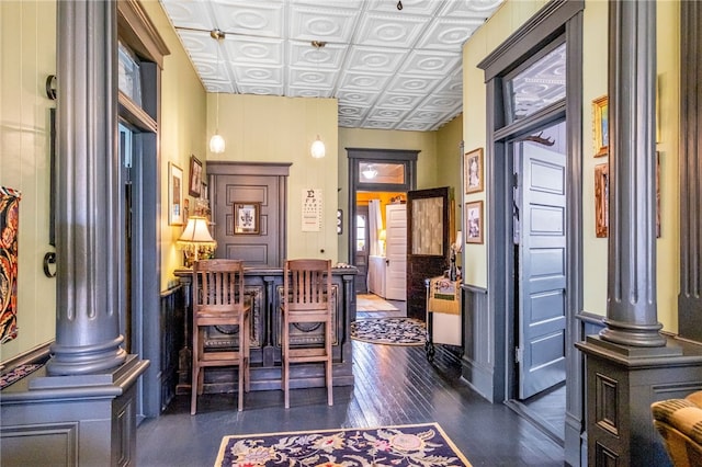 interior space featuring an ornate ceiling, wainscoting, decorative columns, and dark wood-style floors