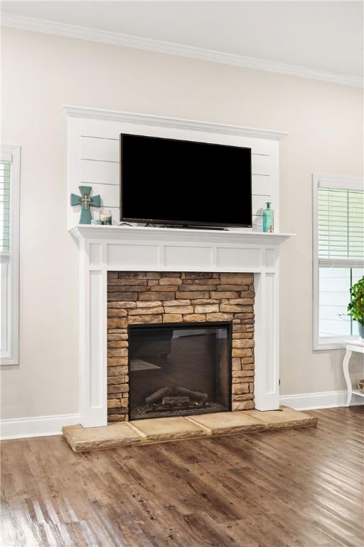 detailed view of a fireplace, baseboards, crown molding, and wood finished floors