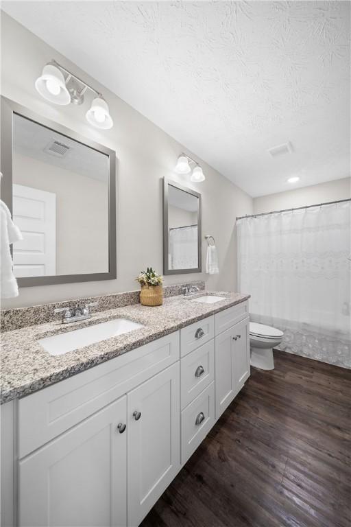 bathroom with toilet, wood finished floors, double vanity, a textured ceiling, and a shower with shower curtain
