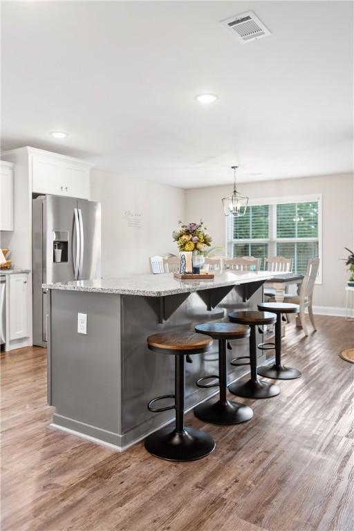 bar area featuring stainless steel fridge with ice dispenser, light wood-type flooring, recessed lighting, decorative light fixtures, and a chandelier