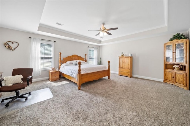 bedroom featuring a raised ceiling, light carpet, baseboards, and ceiling fan