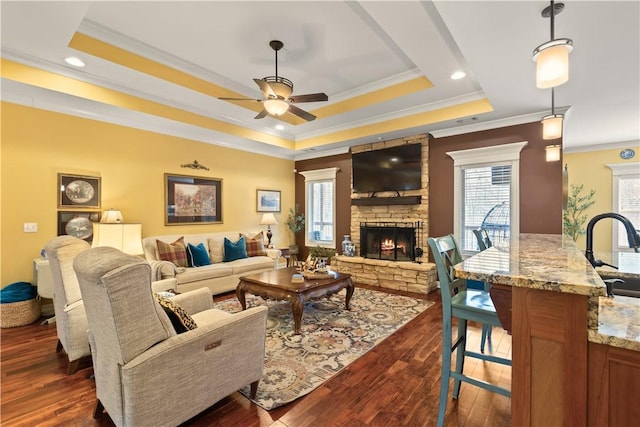 living room with a fireplace, a tray ceiling, a wealth of natural light, and dark hardwood / wood-style floors