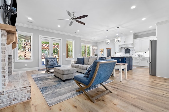 living room featuring a fireplace, light hardwood / wood-style flooring, ceiling fan with notable chandelier, and ornamental molding