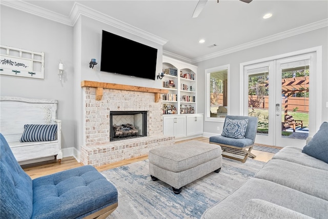 living room with a brick fireplace, hardwood / wood-style flooring, ceiling fan, built in shelves, and ornamental molding