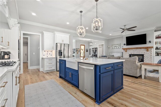 kitchen with a brick fireplace, stainless steel appliances, blue cabinets, a kitchen island with sink, and white cabinets