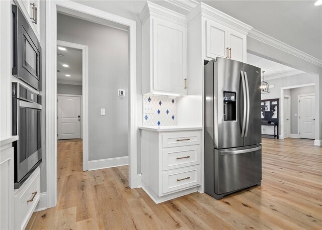 kitchen featuring white cabinets, ornamental molding, appliances with stainless steel finishes, tasteful backsplash, and light hardwood / wood-style floors