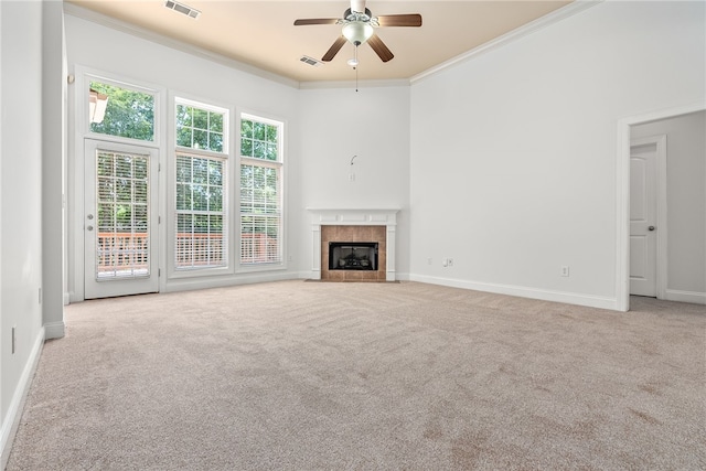 unfurnished living room with a tiled fireplace, ceiling fan, light colored carpet, and ornamental molding