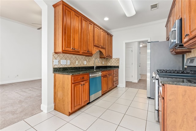 kitchen with appliances with stainless steel finishes, dark stone counters, light colored carpet, and crown molding