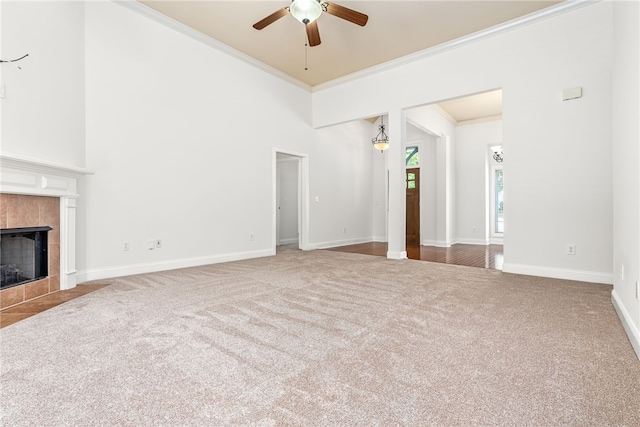 unfurnished living room with carpet floors, ceiling fan, ornamental molding, and a tiled fireplace