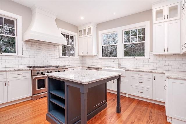 kitchen with light wood-type flooring, high end stove, white cabinetry, and custom exhaust hood