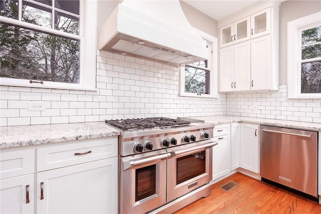 kitchen with stainless steel appliances, white cabinetry, light wood-style floors, ventilation hood, and tasteful backsplash