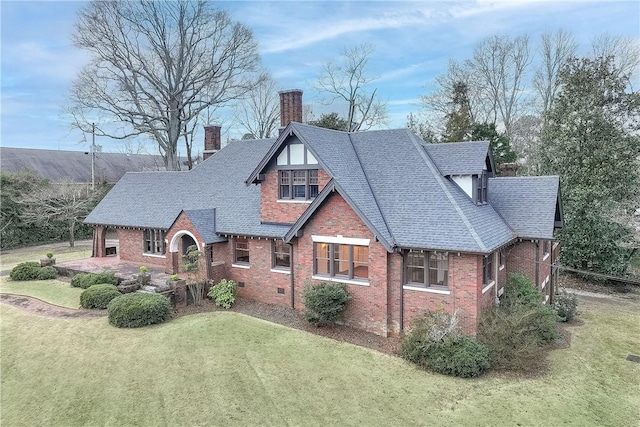 tudor-style house featuring roof with shingles, a front lawn, crawl space, and a chimney