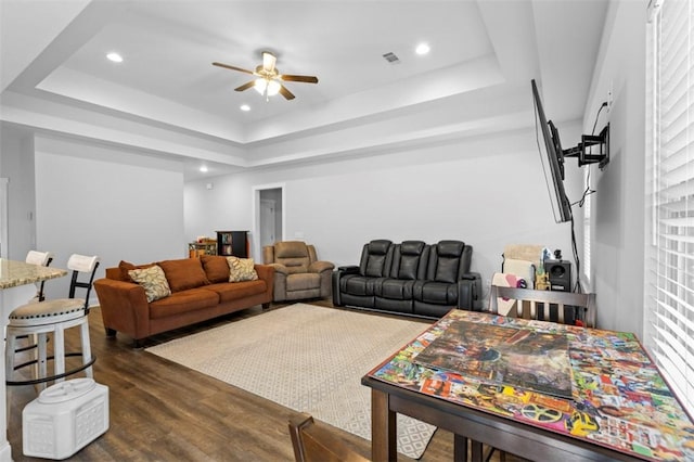 living room featuring dark wood-type flooring, a raised ceiling, and ceiling fan