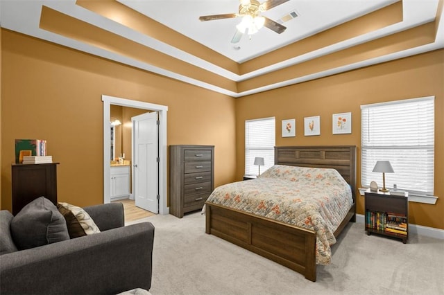 bedroom featuring light colored carpet, a raised ceiling, ceiling fan, and ensuite bathroom