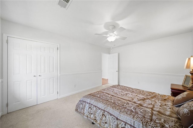 carpeted bedroom featuring a wainscoted wall, a closet, and ceiling fan