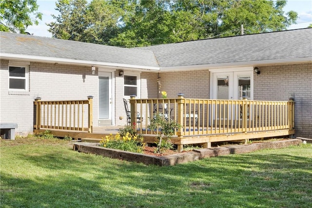 back of property featuring brick siding, a deck, roof with shingles, and a yard