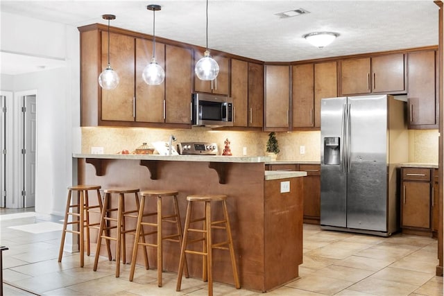 kitchen with appliances with stainless steel finishes, decorative backsplash, a breakfast bar, and a peninsula