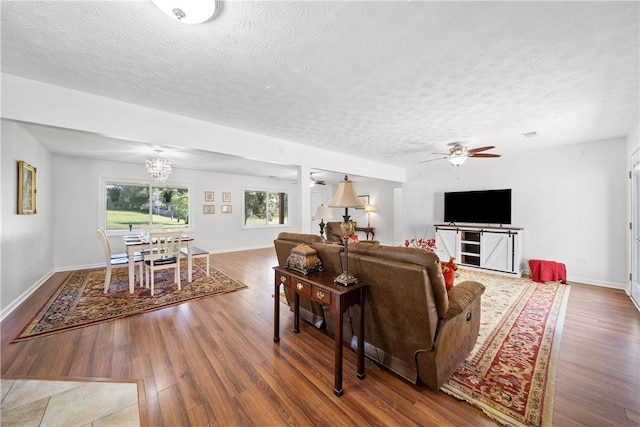 living room with a textured ceiling, ceiling fan with notable chandelier, baseboards, and wood finished floors