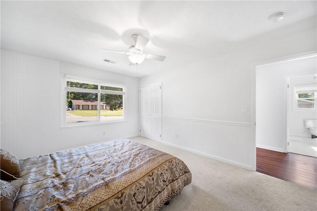 carpeted bedroom with a ceiling fan, a closet, and wainscoting