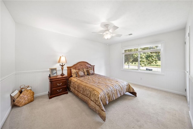 bedroom featuring light carpet, a wainscoted wall, and ceiling fan