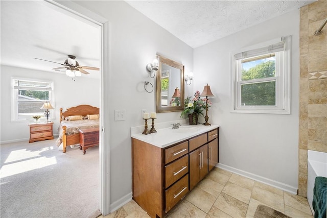 ensuite bathroom with baseboards, vanity, ceiling fan, a tub, and a textured ceiling