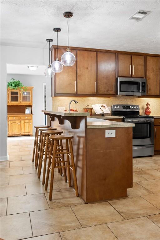 kitchen with a peninsula, decorative light fixtures, visible vents, decorative backsplash, and appliances with stainless steel finishes