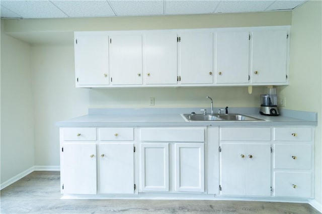 kitchen with a paneled ceiling, white cabinetry, light countertops, and a sink