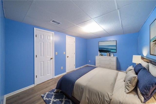 bedroom featuring a paneled ceiling, visible vents, baseboards, and wood finished floors