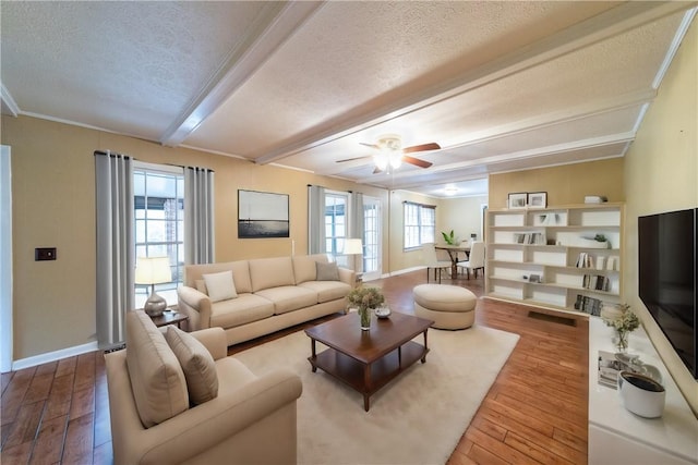 living area featuring a textured ceiling, wood finished floors, baseboards, ornamental molding, and beam ceiling