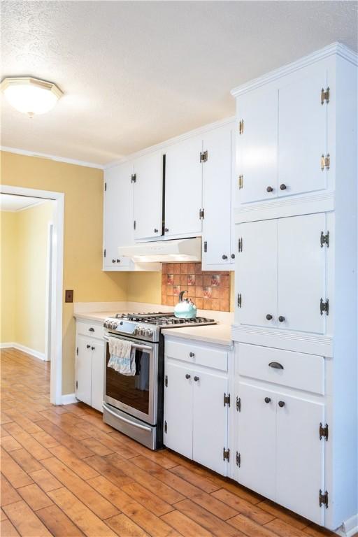 kitchen with stainless steel gas stove, white cabinets, light wood-style floors, light countertops, and under cabinet range hood