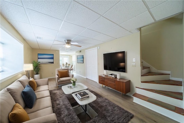 living area with stairway, a drop ceiling, and wood finished floors