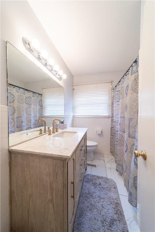 bathroom featuring toilet, marble finish floor, tile walls, and vanity