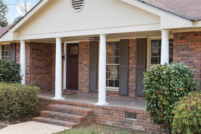 entrance to property with a shingled roof, a porch, and brick siding