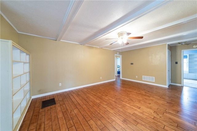 empty room with baseboards, visible vents, beamed ceiling, and wood finished floors