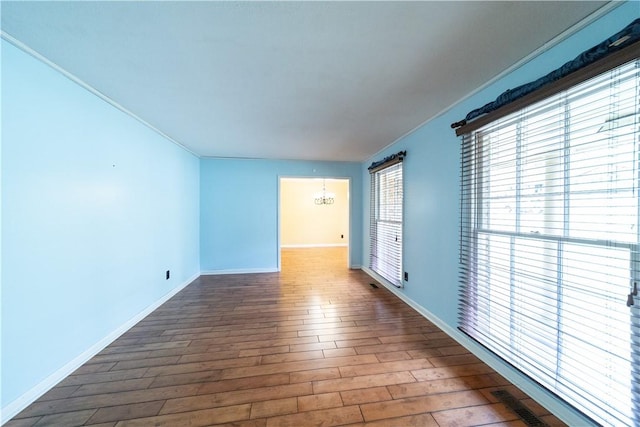 empty room featuring a chandelier, dark wood-style flooring, visible vents, and baseboards