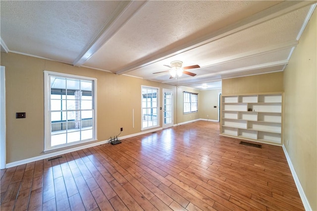 spare room featuring a textured ceiling, visible vents, beamed ceiling, and wood finished floors