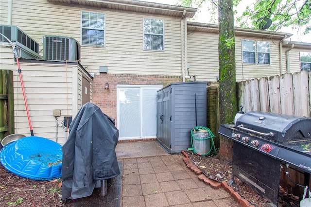 rear view of house with central air condition unit, fence, and brick siding