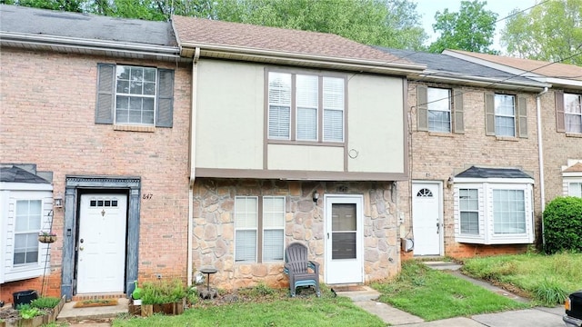 townhome / multi-family property featuring brick siding, a shingled roof, stucco siding, and stone siding