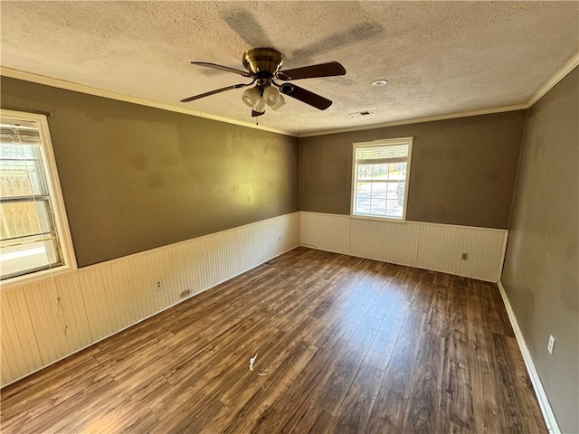 empty room with a wainscoted wall, wood finished floors, a textured ceiling, crown molding, and a ceiling fan