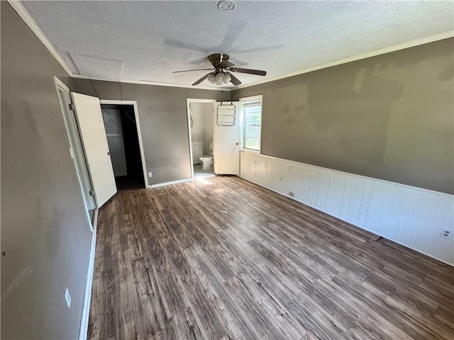 unfurnished bedroom with a textured ceiling, wood finished floors, a wainscoted wall, ornamental molding, and a closet