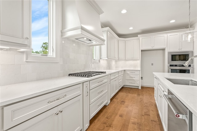 kitchen featuring pendant lighting, custom exhaust hood, white cabinets, sink, and stainless steel appliances