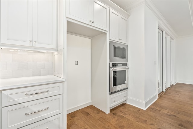 kitchen featuring ornamental molding, stainless steel oven, built in microwave, light hardwood / wood-style flooring, and white cabinetry