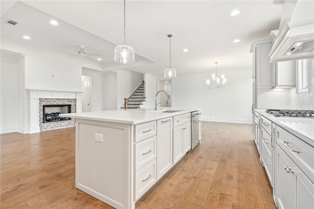 kitchen featuring sink, decorative light fixtures, white cabinetry, and an island with sink