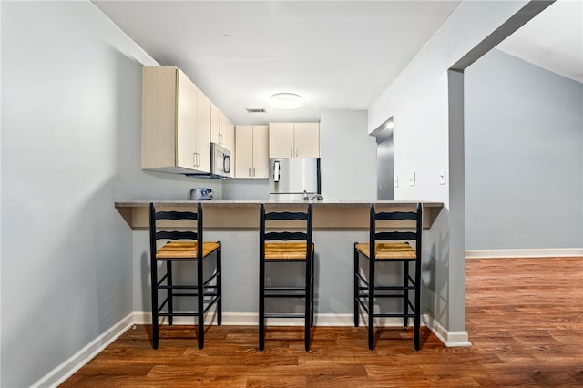 601 N Gay St Unit 202, Auburn, AL 36830 - kitchen with freestanding refrigerator, stainless steel microwave, a peninsula, wood finished floors, and a kitchen breakfast bar