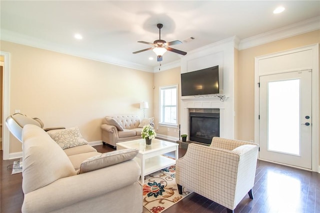 living room featuring ceiling fan, ornamental molding, dark wood-type flooring, and a tiled fireplace