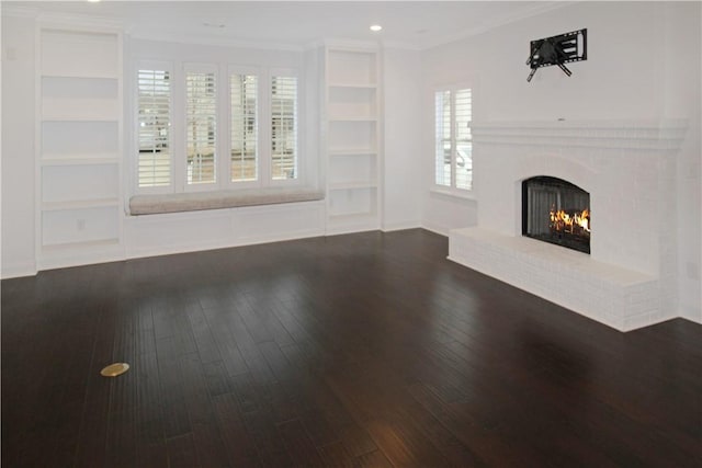 unfurnished living room featuring a brick fireplace, built in shelves, dark hardwood / wood-style flooring, and a healthy amount of sunlight