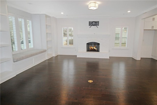 unfurnished living room with built in features, a brick fireplace, crown molding, and dark hardwood / wood-style flooring