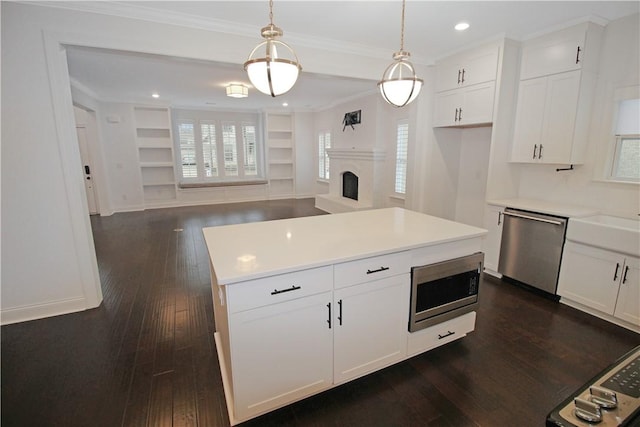 kitchen with decorative light fixtures, a kitchen island, white cabinets, and appliances with stainless steel finishes