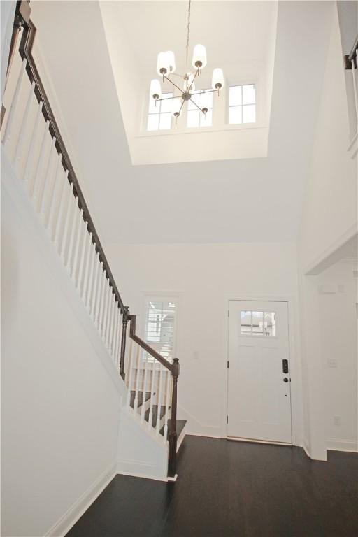 foyer featuring dark wood-type flooring, a towering ceiling, and an inviting chandelier